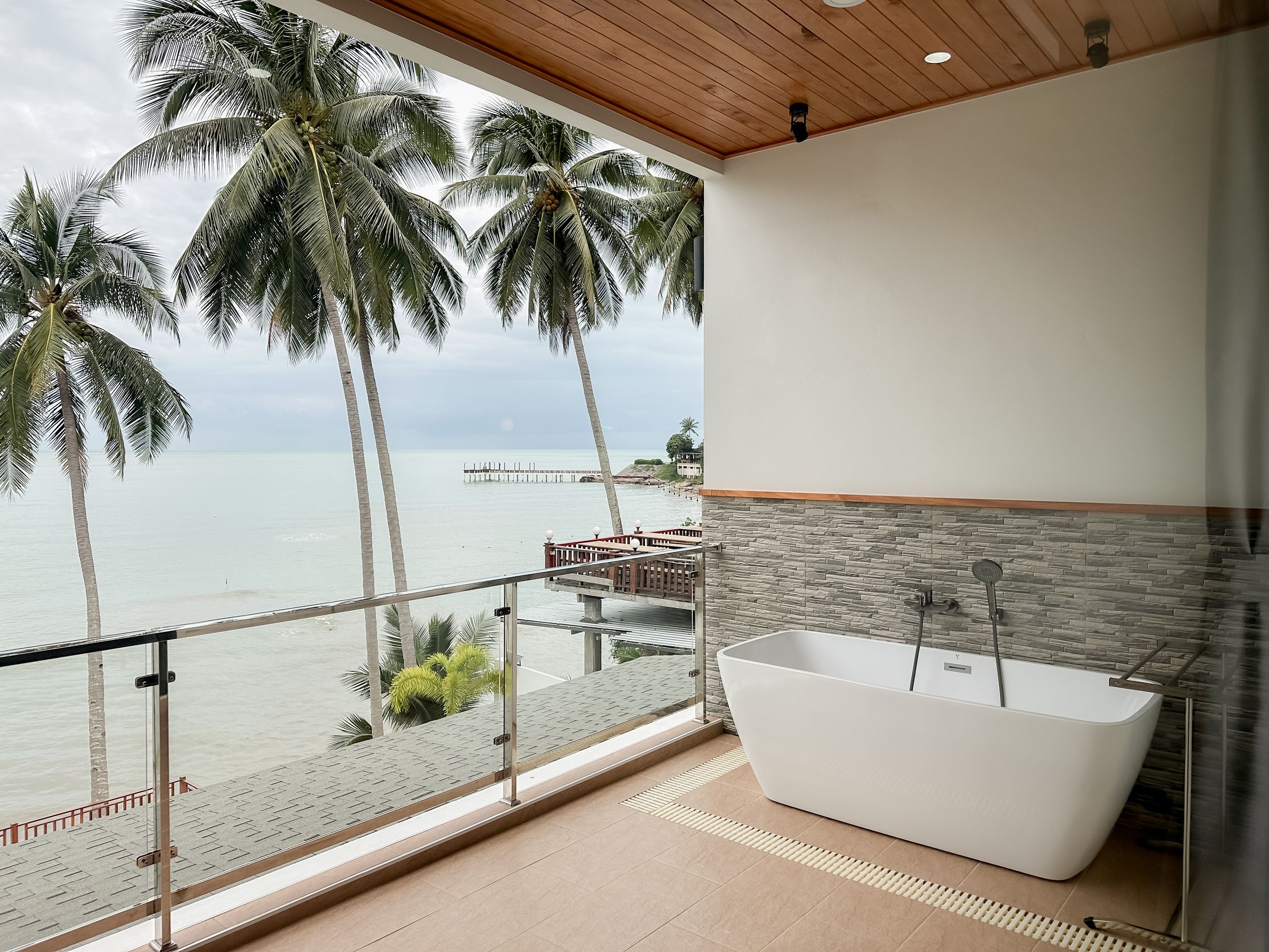 Freestanding bathtub on a balcony overlooking the sea and coconut palms